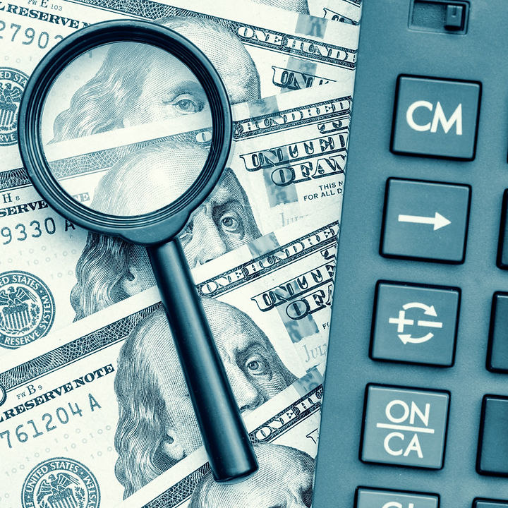 Close-up of a calculator and dollar bills above a magnifying glass.